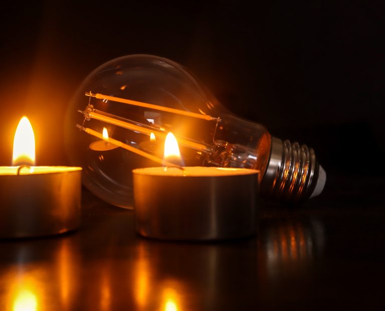 Loadshedding or power cuts, blackout concept. Light bulb with candles in the foreground