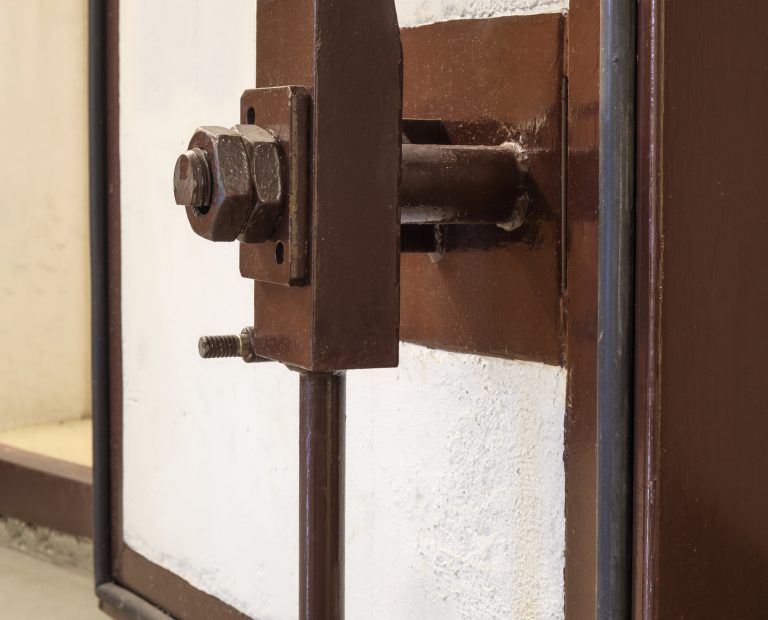 Massive heavy duty air-lock on concrete door in fallout shelter or survival bunker used during war or disaster. Selective focus.